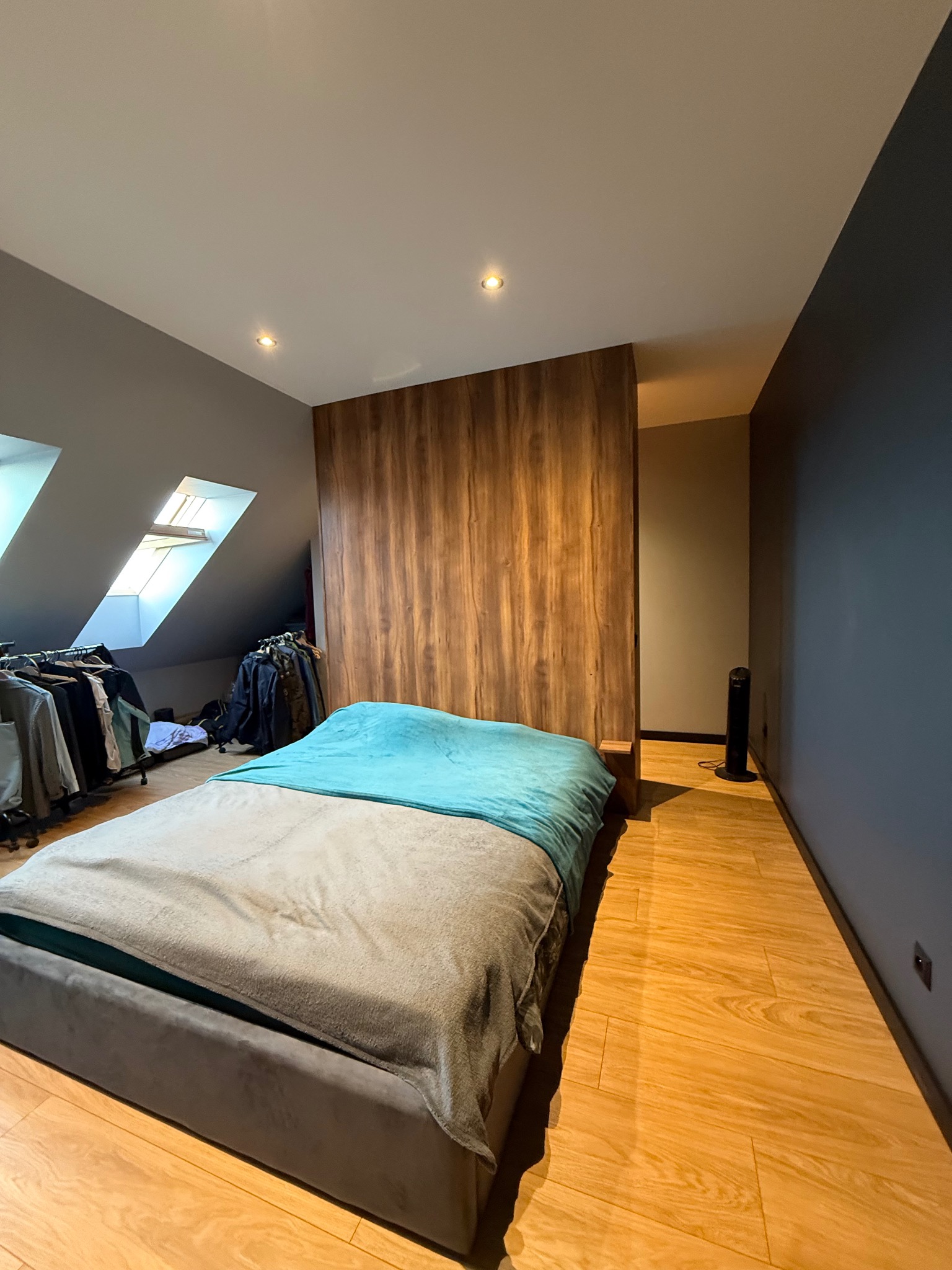 Szafa wnękowa z drewnianymi frontami, oddzielająca przestrzeń sypialną w pokoju na poddaszu. Widoczne skosy, okna dachowe i podłoga z paneli.