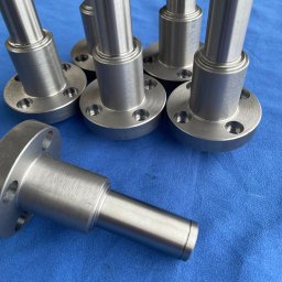 WIMAT Obróbka skrawaniem Mateusz Krawczyk - Srebrne, metalowe elementy z kołnierzami i otworami na niebieskim tle. Precyzyjnie wykonane detale, widoczne ślady obróbki. Elementy gotowe do montażu.