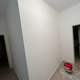 NOWE GORYZONTY SPÓŁKA Z OGRANICZONĄ ODPOWIEDZIALNOŚCIĄ - Świeżo pomalowane na biało ściany w korytarzu, widoczna puszka z farbą na podłodze zabezpieczonej folią. Ujęcie z dołu, podkreślające gładkość powierzchni.