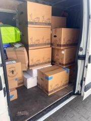 Wnętrze białego busa wypełnione kartonowymi pudłami różnej wielkości, niektóre z nadrukiem, sugerujące transport lub przeprowadzkę. Widoczne zabezpieczenia ładunku.