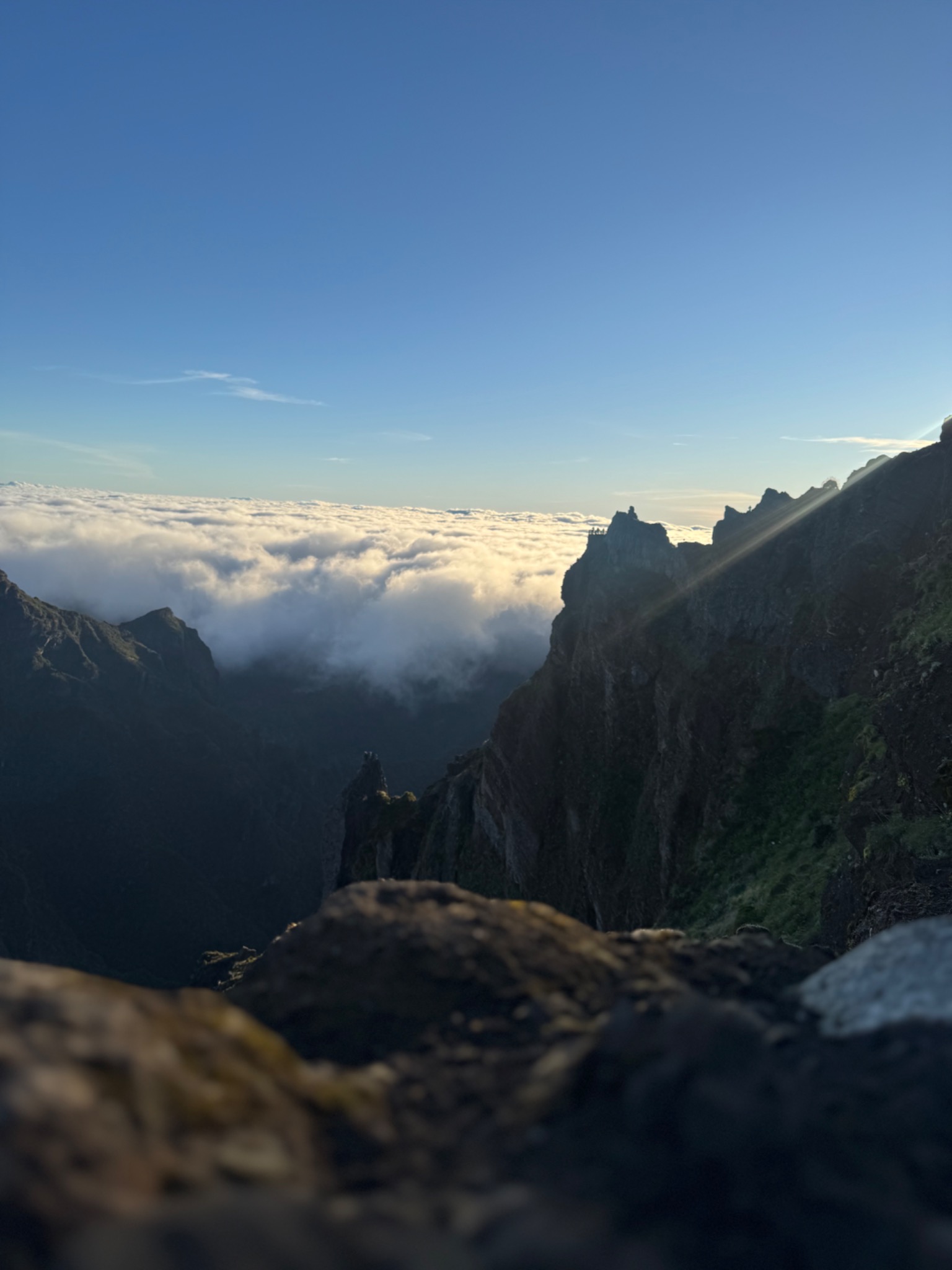 Malowniczy widok z góry na morze chmur, z ostrymi szczytami gór wystającymi ponad nie. W tle błękitne niebo. Ujęcie z bliska na skaliste podłoże.