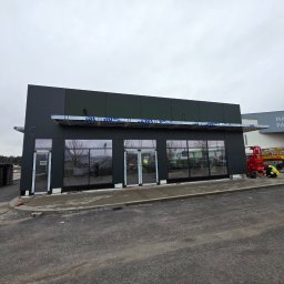 V.S.E.G. Sp. z o.o. - Nowoczesny budynek w trakcie budowy, prawdopodobnie restauracja, z widocznymi elementami instalacji elektrycznej i pracującym elektrykiem w odblaskowej kamizelce.