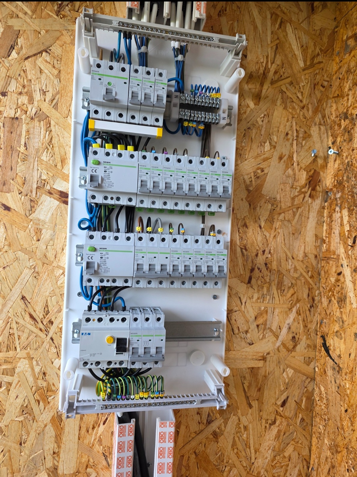 Rozdzielnica elektryczna NOARK i EATON zamontowana na ścianie z płyty OSB. Widoczne zabezpieczenia, przewody i listwy. Estetyczne i profesjonalne wykonanie.