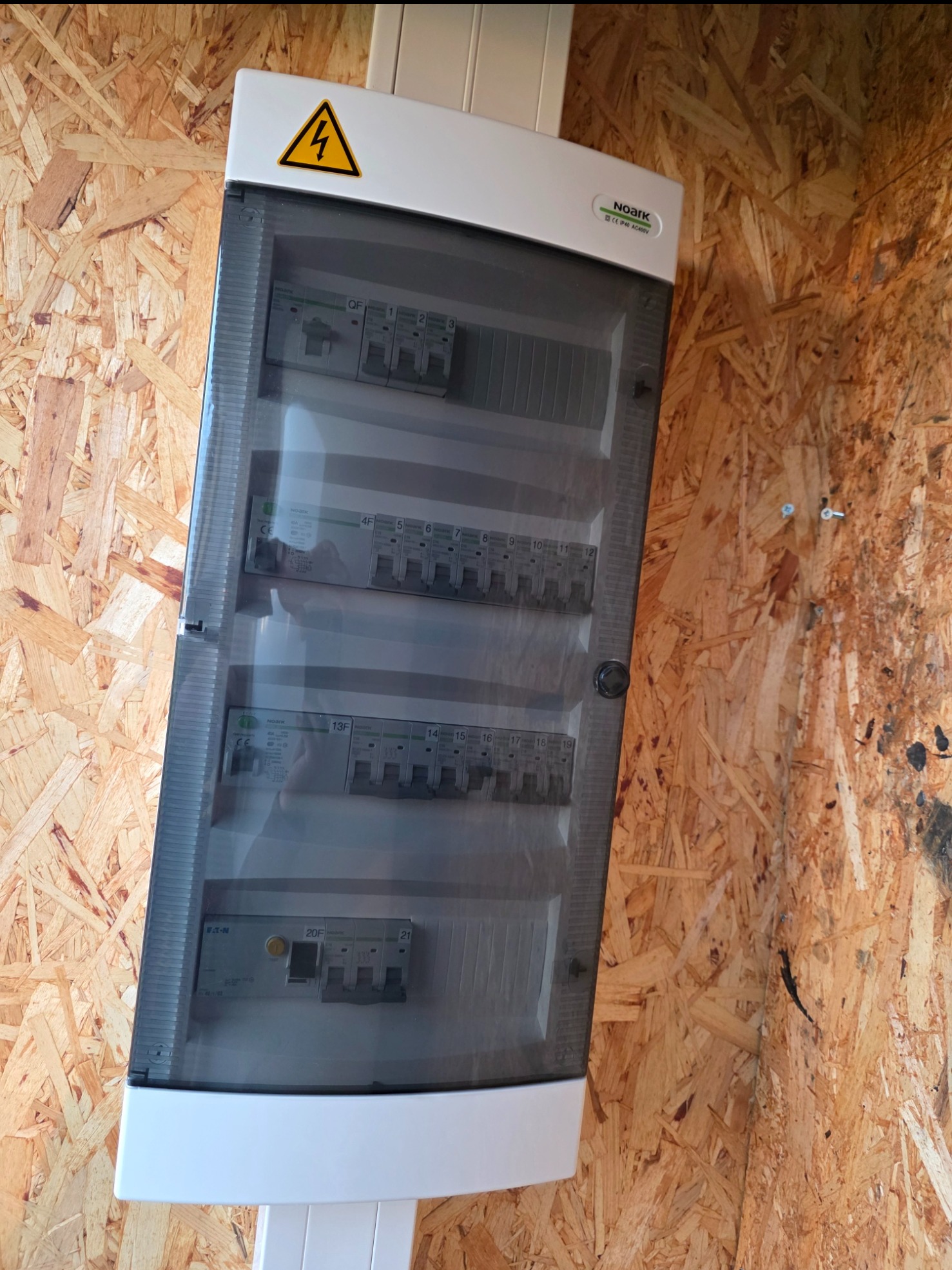 Rozdzielnica elektryczna Noark z bezpiecznikami, zamontowana na ścianie z płyty OSB. Widoczny symbol ostrzegawczy. Instalacja elektryczna wewnątrz skrzynki.