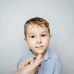 Wera Wysk Fotografia - Portret chłopca w błękitnej koszuli, z dłonią podtrzymującą jego podbródek, na jasnym tle. Ujęcie z bliska, skupione na twarzy dziecka.