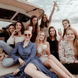 Wera Wysk Fotografia - Grupa uśmiechniętych kobiet świętuje na jachcie, trzymając kieliszki i butelkę Moët & Chandon. Ujęcie z bliska, z widokiem na wodę w tle.