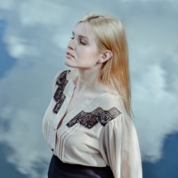 Wera Wysk Fotografia - Portret kobiety o jasnych włosach, w bluzce z koronkowymi wstawkami, na tle nieba odbijającego się w wodzie. Ujęcie z profilu, delikatne światło.