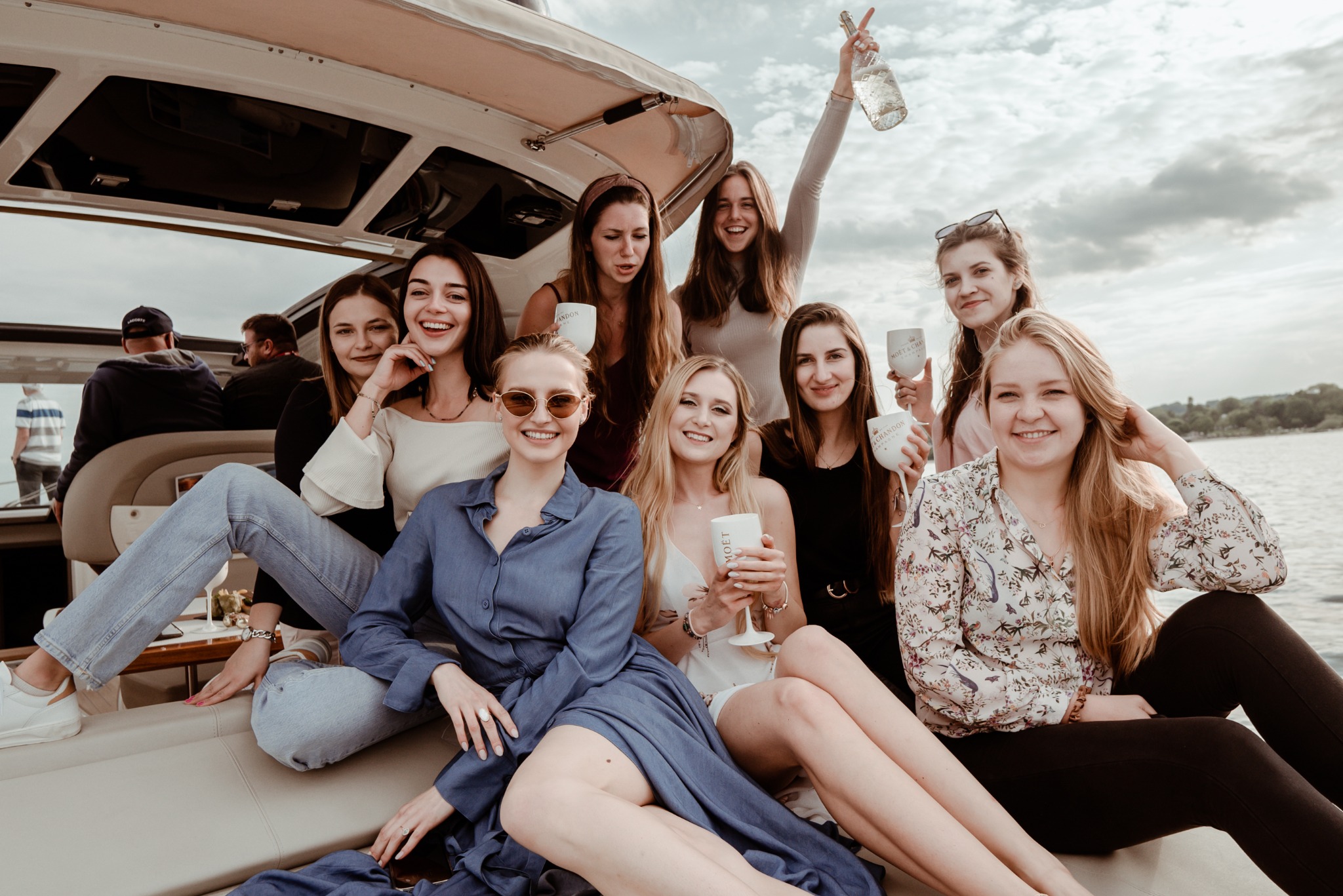Grupa uśmiechniętych kobiet świętuje na jachcie, trzymając kieliszki i butelkę Moët & Chandon. Ujęcie z bliska, z widokiem na wodę w tle.