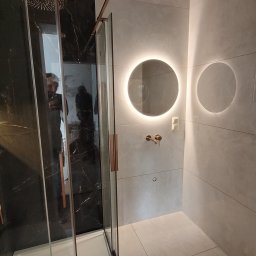 MP CONCEPT Marcin Pawelec - Nowoczesna łazienka z kabiną prysznicową typu walk-in, czarnymi płytkami imitującymi marmur i okrągłym lustrem z podświetleniem LED. Minimalistyczny design.