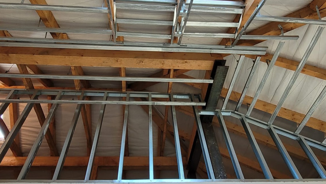 Szkielet poddasza z metalowych profili, widoczne drewniane belki stropowe i izolacja. Konstrukcja przygotowana pod montaż płyt karton-gips.