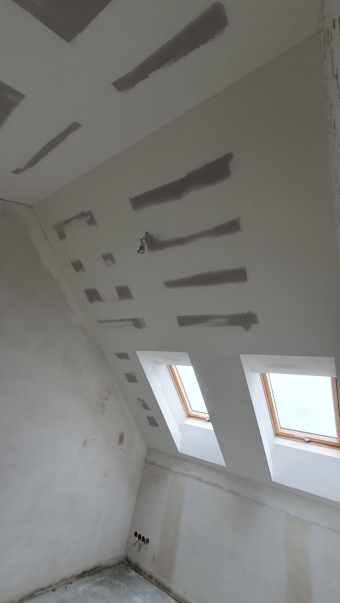 Poddasze ze skosami w trakcie szpachlowania. Widoczne okna dachowe i fragment instalacji elektrycznej. Ściany i sufit przygotowane do malowania.