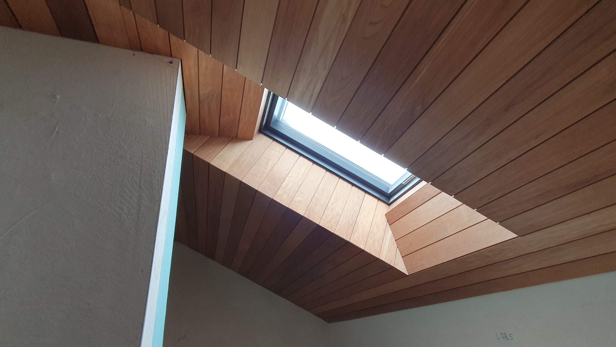 Drewniana boazeria na skośnym poddaszu z oknem dachowym, widok z dołu. Fragment ściany w surowym tynku. Naturalne oświetlenie.