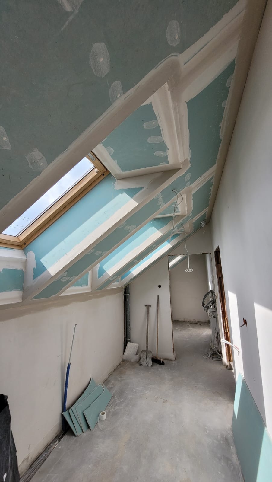 Poddasze z oknami dachowymi w trakcie montażu płyt gipsowo-kartonowych. Widoczne narzędzia i materiały budowlane. Surowe wykończenie, przygotowanie do dalszych prac.