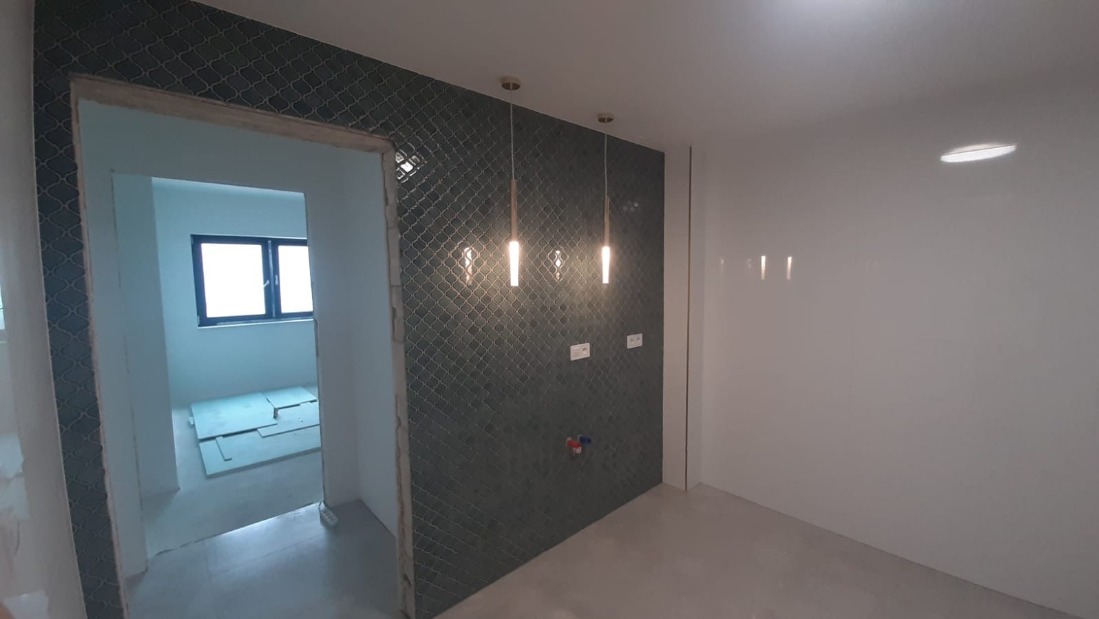 Wykończona ściana z mozaiką w łazience, widoczne trzy wiszące lampy. W tle widoczne płyty kartonowo-gipsowe w pomieszczeniu obok.