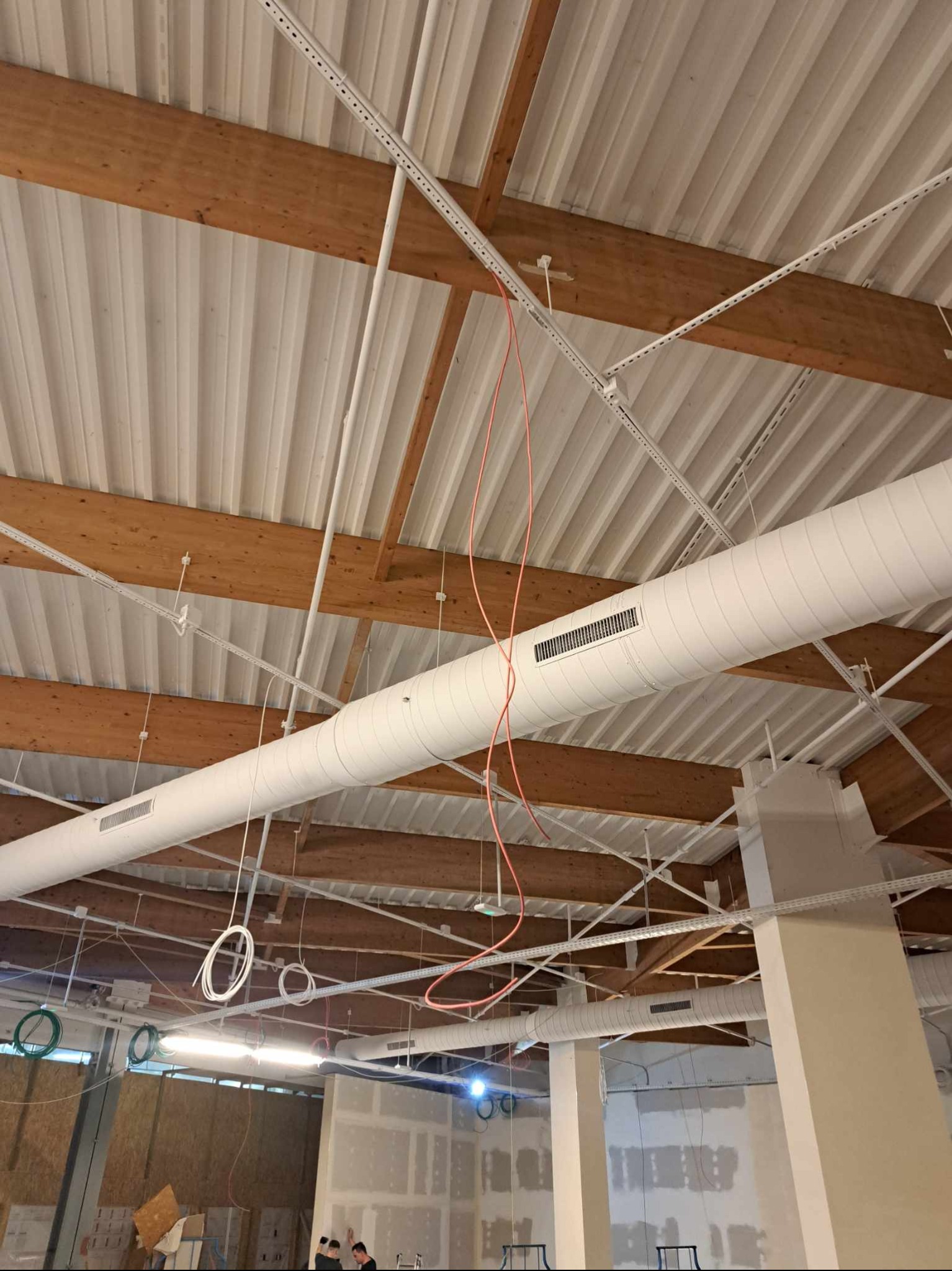Montaż przewodów i instalacji pod sufitem w Jedlińsku. Widoczne kable, rury wentylacyjne i drewniane elementy konstrukcyjne. Prace instalacyjne w obiekcie komercyjnym.