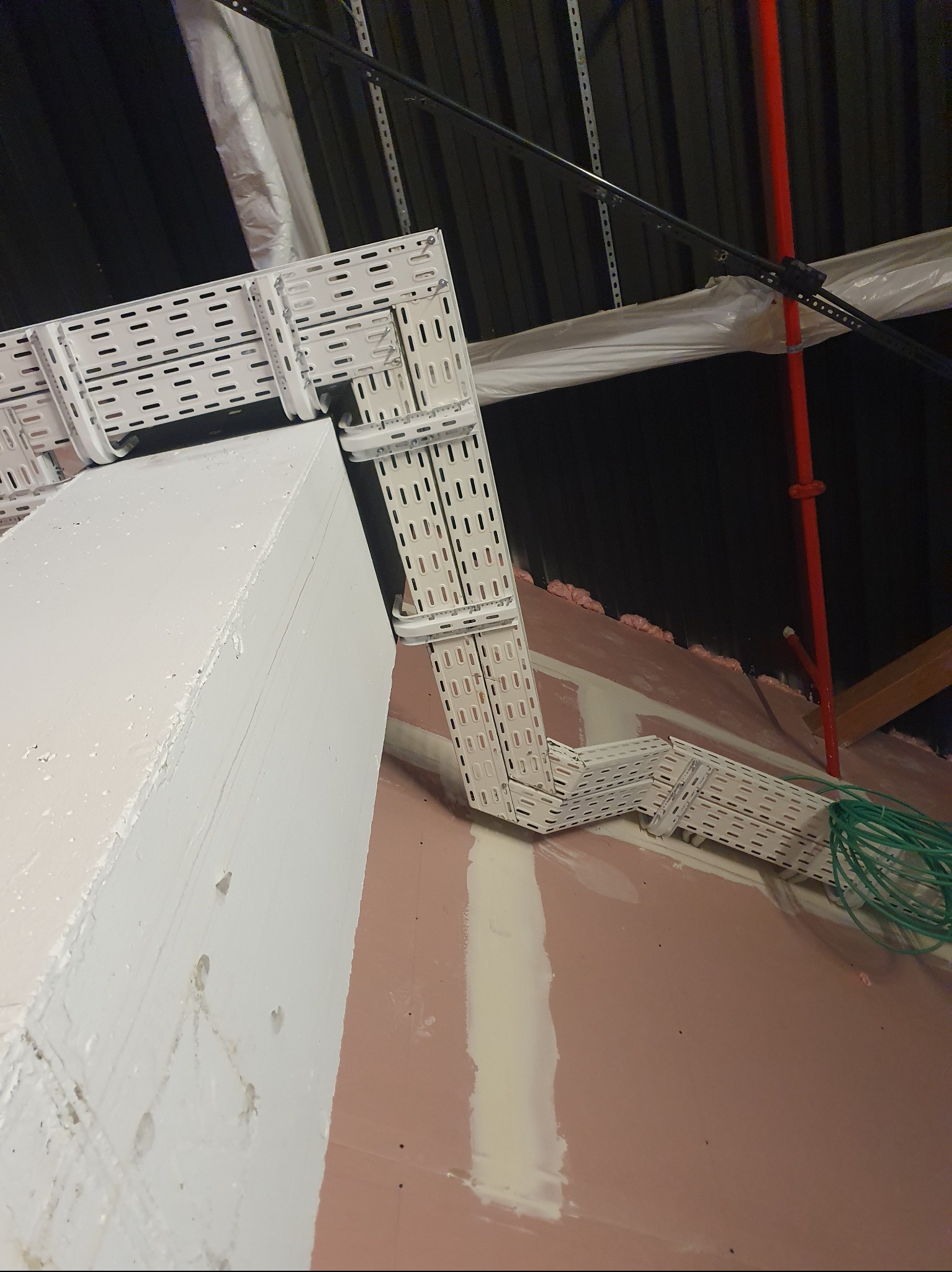 Białe korytka kablowe zamontowane w rogu pomieszczenia, widoczne przewody i elementy konstrukcyjne. Ujęcie z dołu, podkreślające precyzję wykonania.