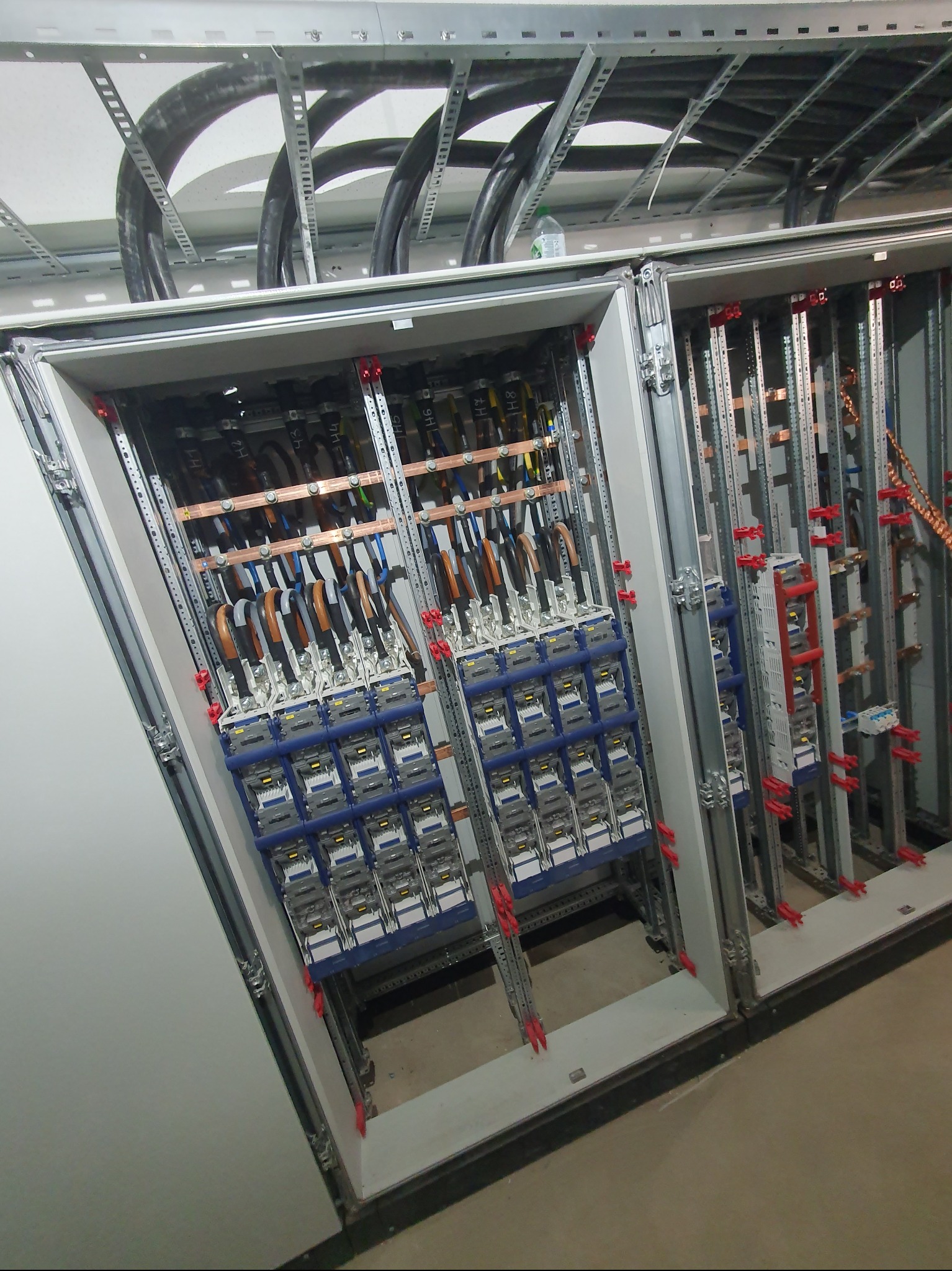 Rozdzielnia elektryczna z widocznymi zabezpieczeniami, przewodami i szynami montażowymi. Widok z dołu, ukazujący szczegółowe połączenia i elementy instalacji.