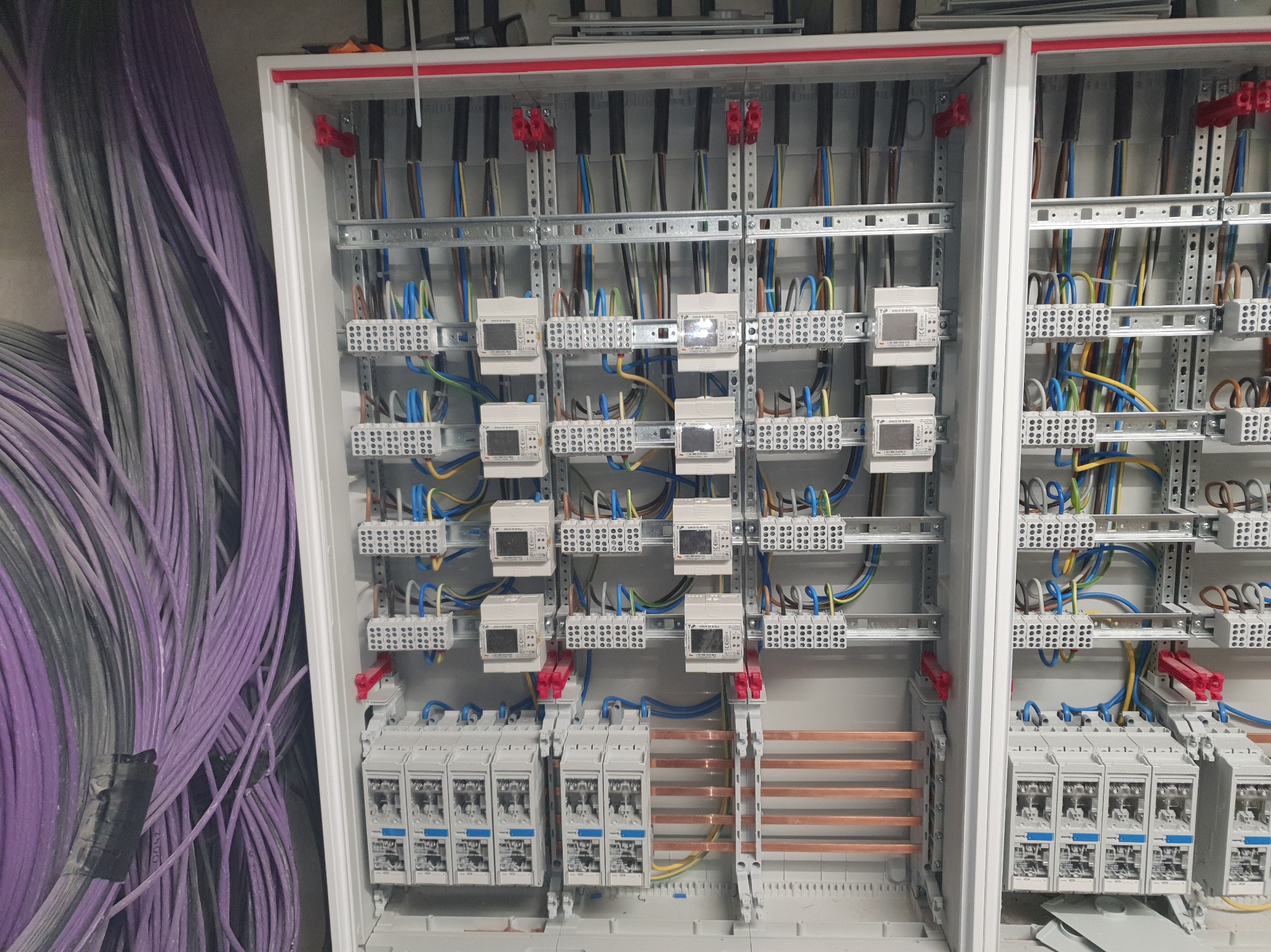 Rozdzielnica elektryczna z zainstalowanymi licznikami i zabezpieczeniami, widoczne kable w kolorach. Profesjonalny montaż w skrzynce z szynami DIN.