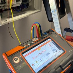 ENERGY - Pomiar impedancji pętli zwarcia ZL-PE miernikiem Sonel MPI-540-PV w rozdzielnicy elektrycznej. Widoczne przewody pomiarowe i drabina Krause w tle.