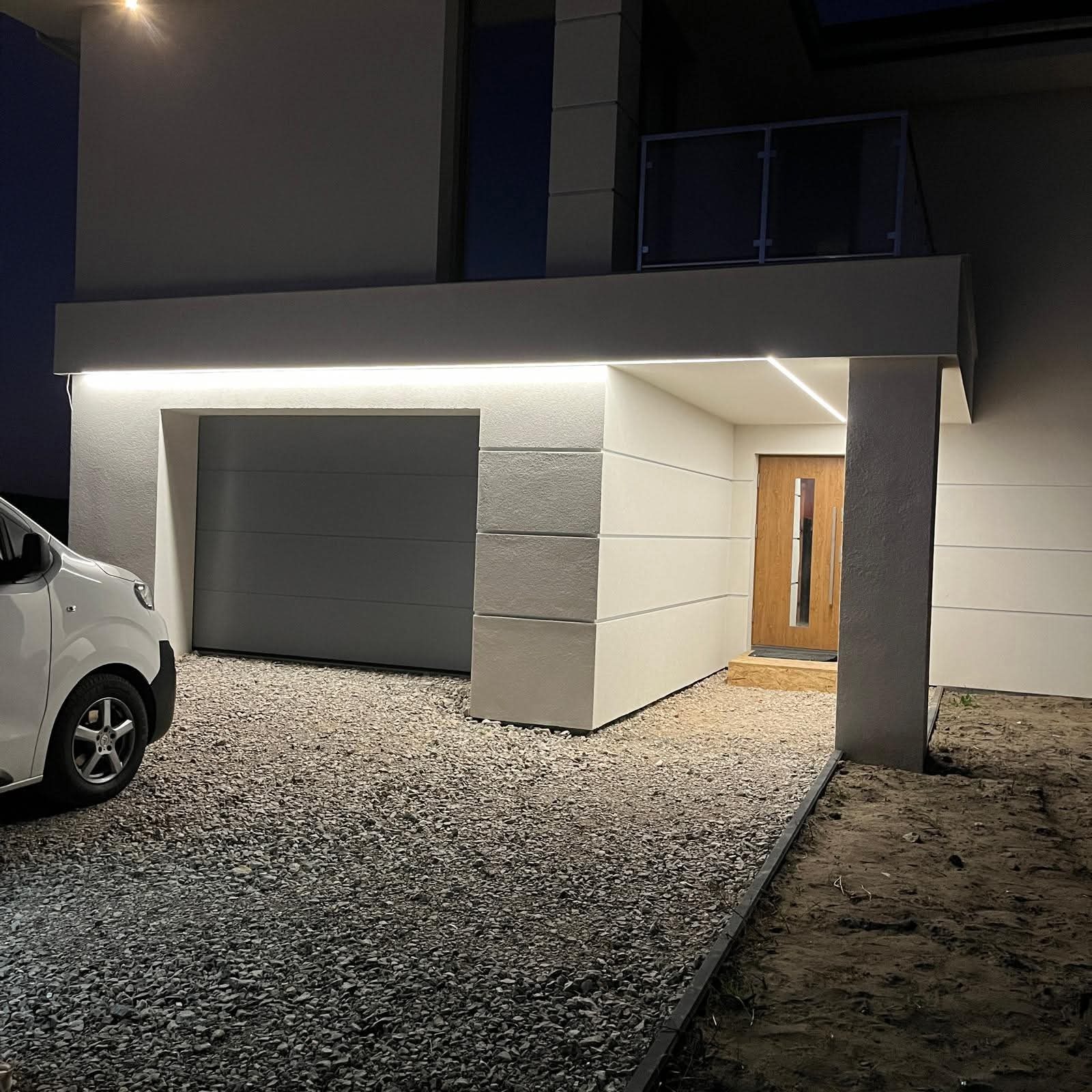 Nowoczesny dom jednorodzinny z garażem i oświetleniem zewnętrznym LED, widoczny samochód. Minimalistyczny design, nocne ujęcie.