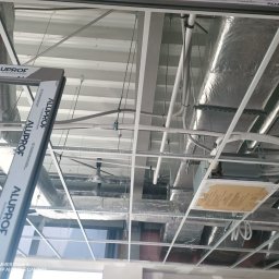 Usługi Transportowe - Sufit podwieszany z widoczną konstrukcją metalową, instalacją wentylacyjną i przewodami. Widoczne profile Aluporf. Ujęcie z dołu, perspektywa z wnętrza budynku.