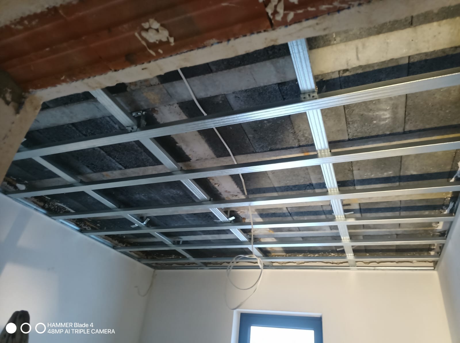 Montaż metalowej konstrukcji sufitu podwieszanego z widocznymi przewodami elektrycznymi, przygotowanie do montażu płyt gipsowo-kartonowych.