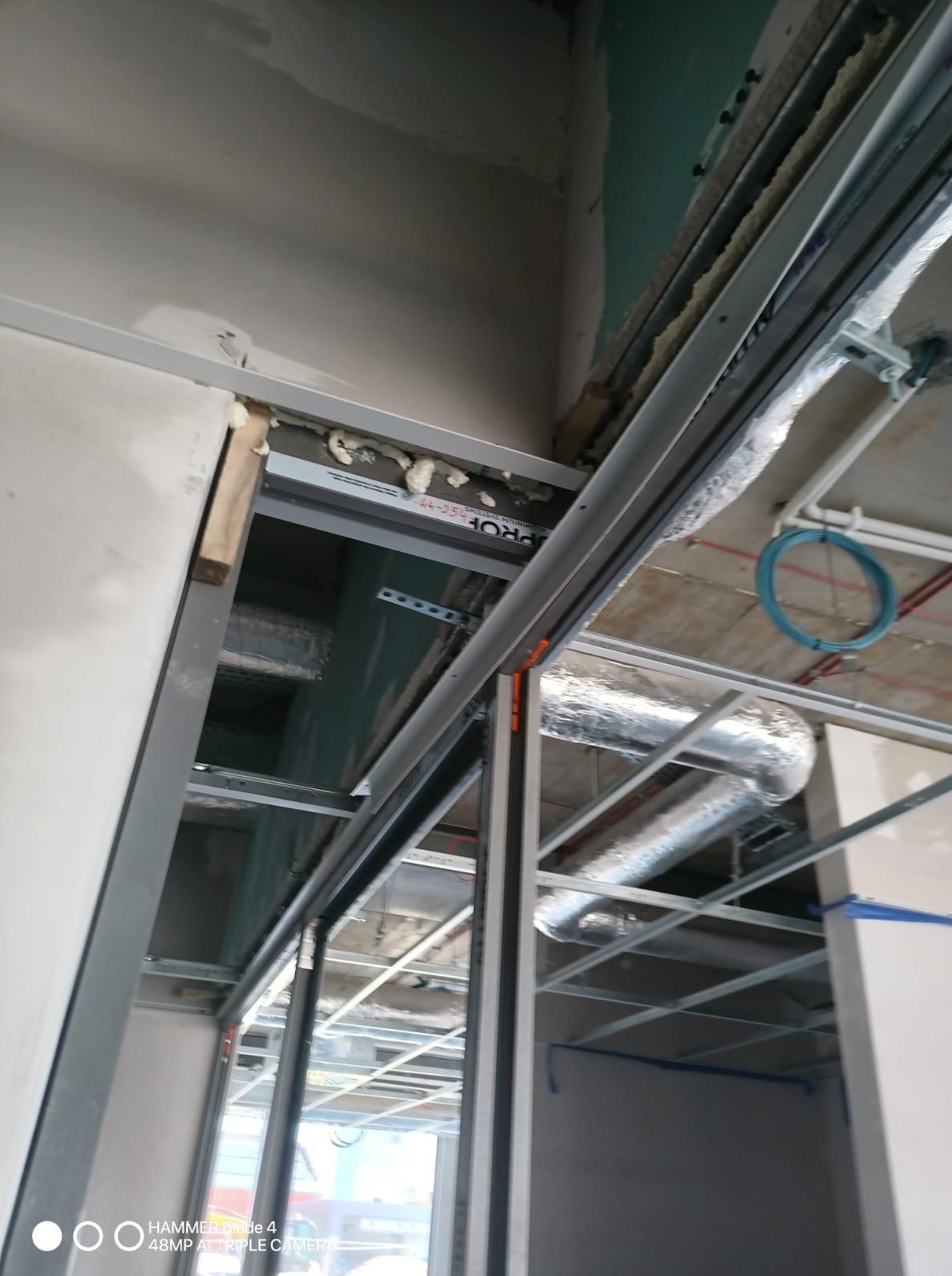 Montaż metalowej konstrukcji sufitu podwieszanego z widocznymi elementami izolacji i instalacji wentylacyjnej. Prace wykończeniowe w trakcie realizacji.