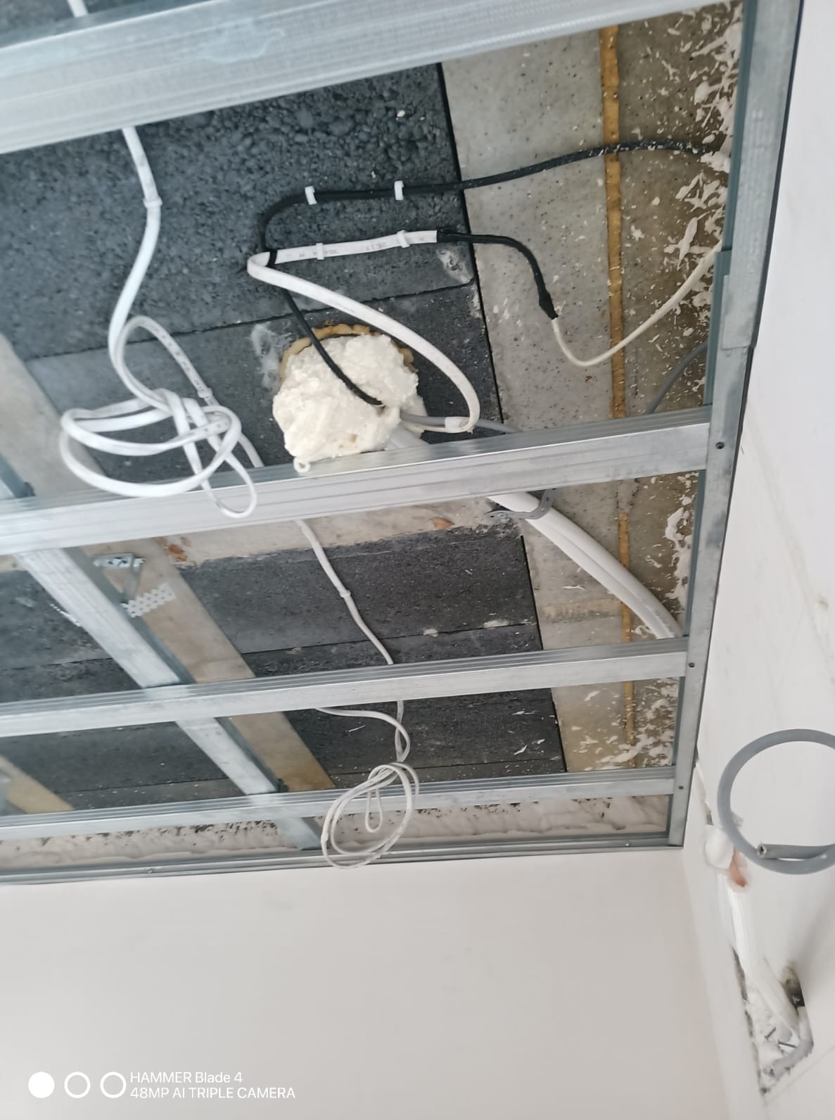 Montaż sufitu podwieszanego z widoczną konstrukcją metalową, izolacją i przewodami. Detal instalacji przed zakryciem płytami.