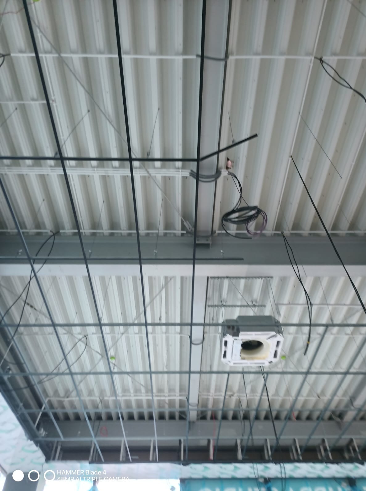 Montaż sufitu podwieszanego z widoczną instalacją elektryczną i klimatyzacją. Metalowa konstrukcja, przewody i elementy wentylacyjne w surowym stanie.