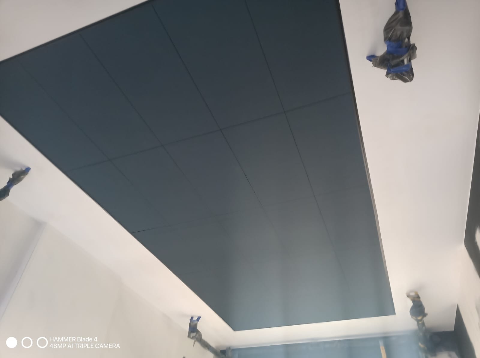 Pomysłowo pomalowany sufit na ciemny kolor, z wyraźnymi liniami podziału na panele. Widoczne zabezpieczenia taśmą malarską przy ścianach.