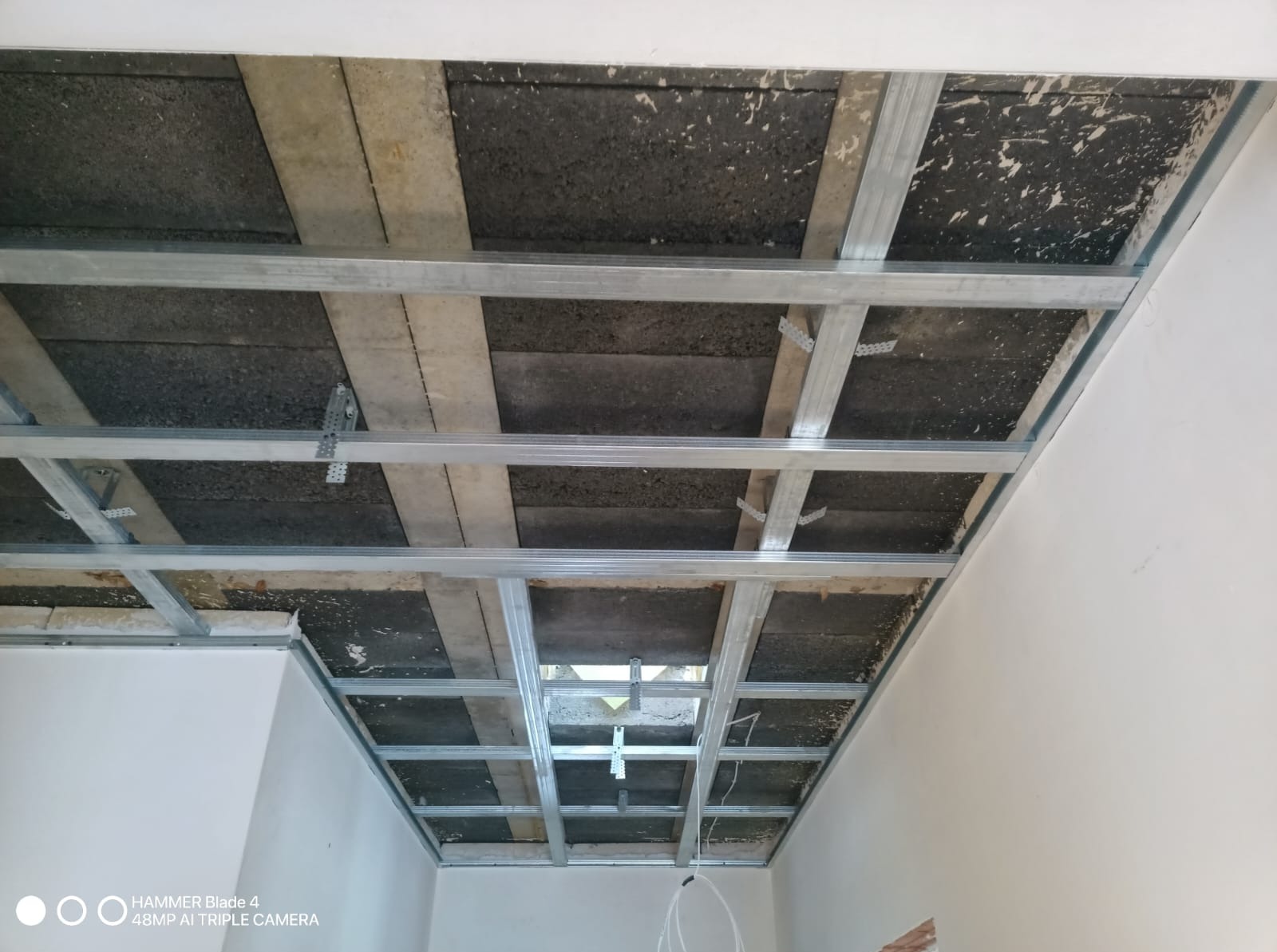 Metalowa konstrukcja sufitu podwieszanego z widoczną izolacją, przygotowana do montażu płyt. Widok z dołu, sufit w trakcie prac wykończeniowych.