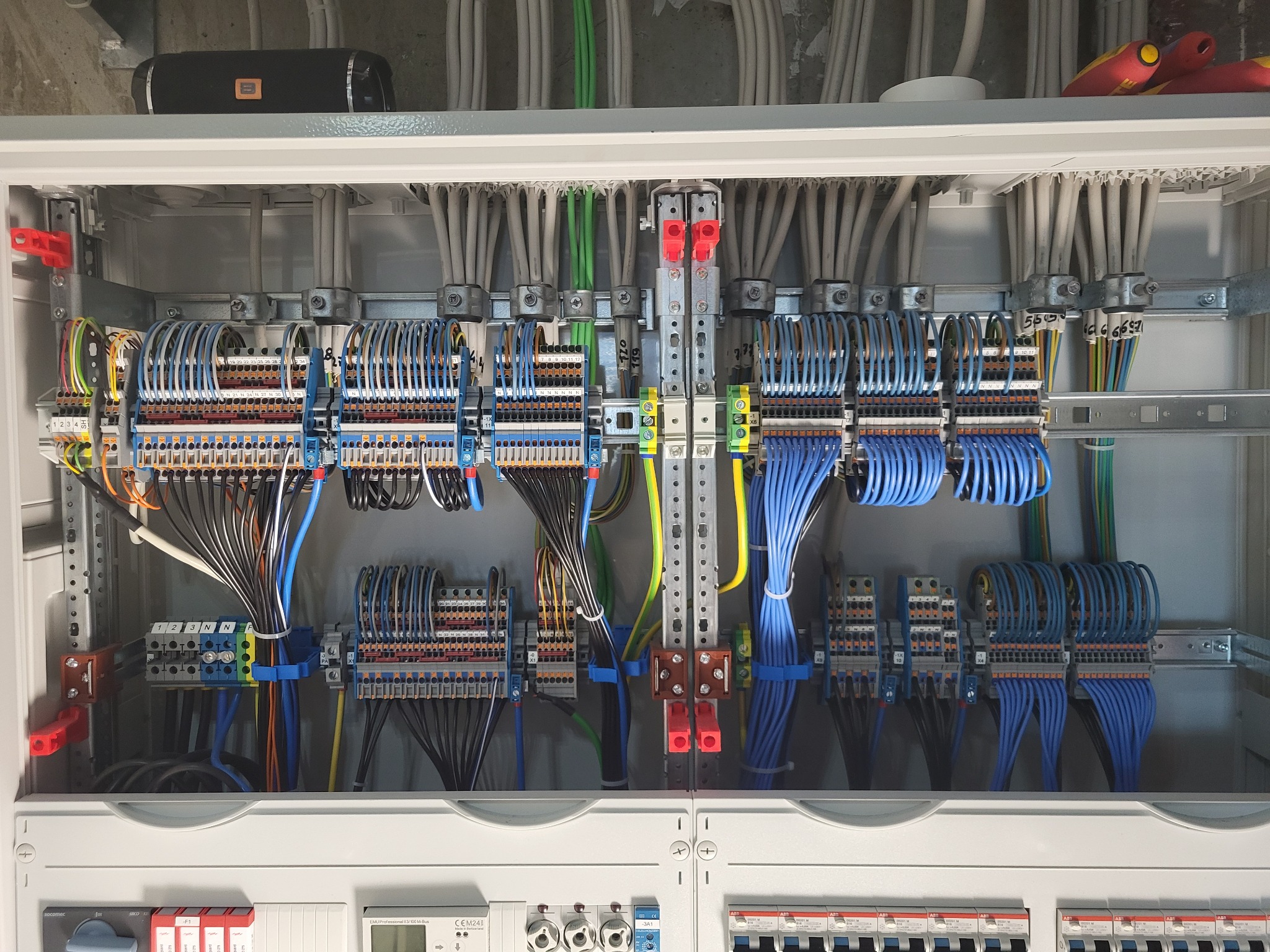 Rozdzielnia elektryczna w szafie, widoczne liczne przewody uporządkowane w wiązki, złącza i zabezpieczenia. Estetyczne ułożenie kabli w kolorach: szarym, niebieskim, zielonym i czarnym.