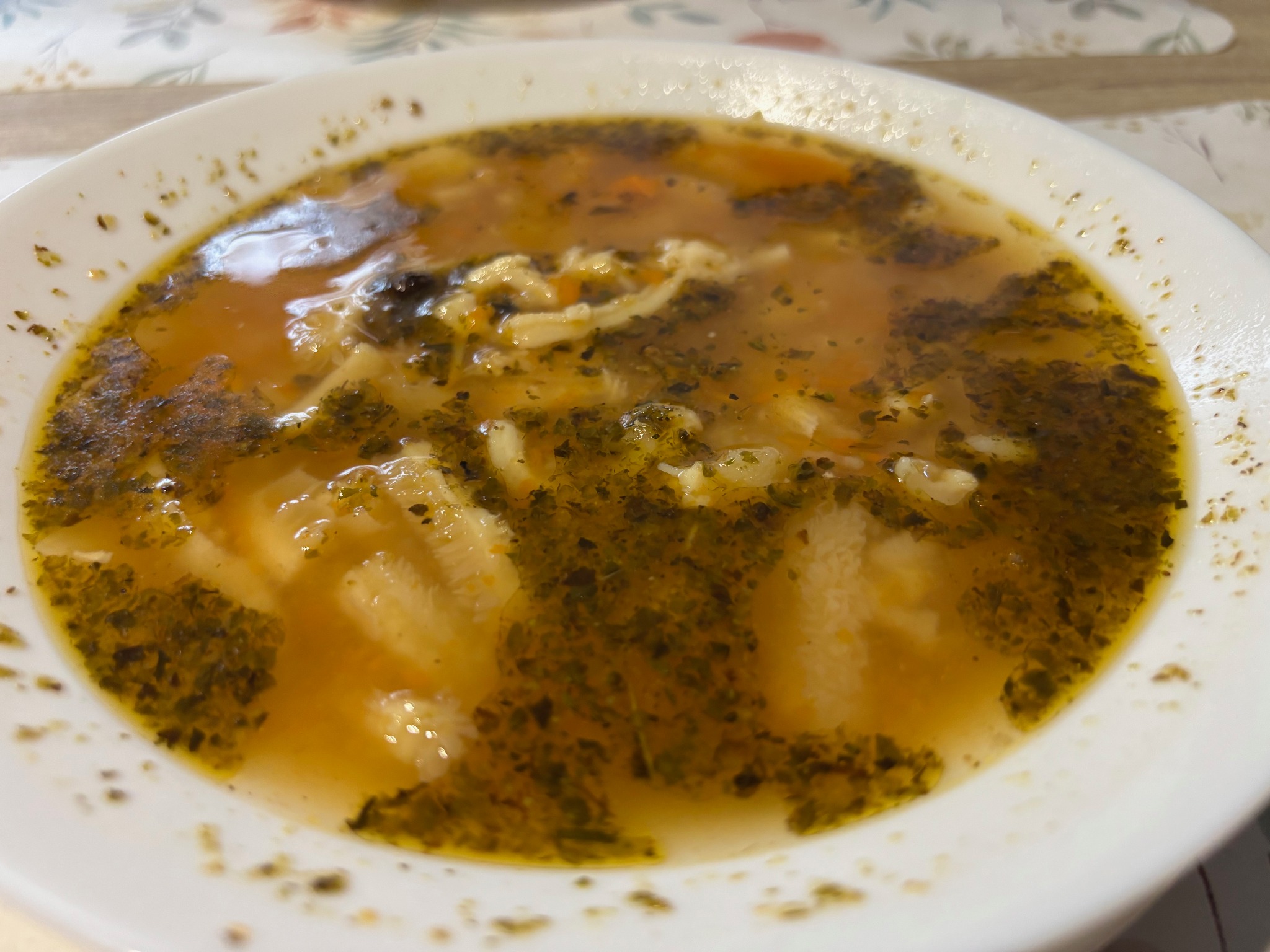 Aromatyczny rosół z makaronem i zielonymi przyprawami w białym talerzu, gotowy do podania. Idealny na catering firmowy lub świąteczny.