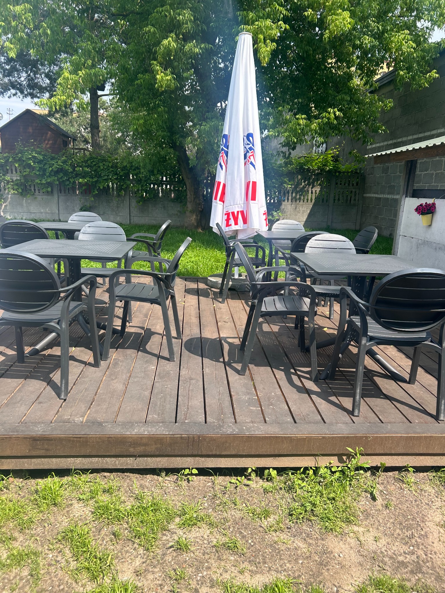 Zewnętrzny taras z czarnymi stolikami i krzesłami pod parasolem w Żyrardowie. Idealne miejsce na catering firmowy lub świąteczny na świeżym powietrzu.