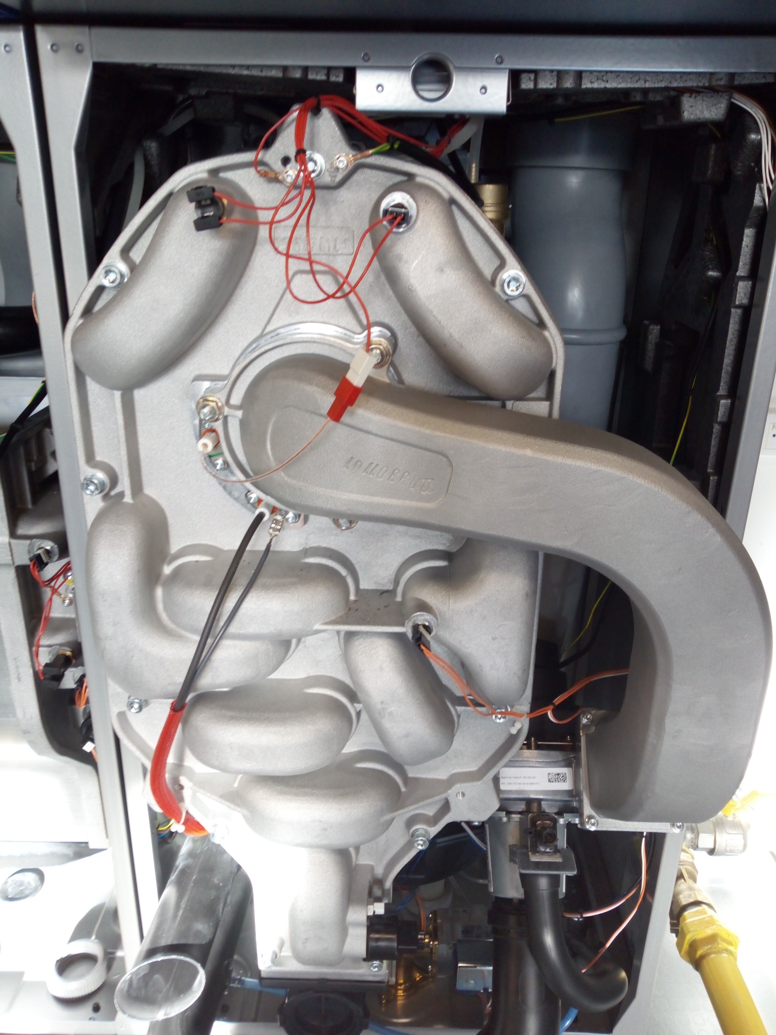 Wnętrze kotła gazowego z widocznymi elementami instalacji, przewodami i podzespołami. Detal techniczny z bliska, ukazujący skomplikowaną budowę urządzenia grzewczego.