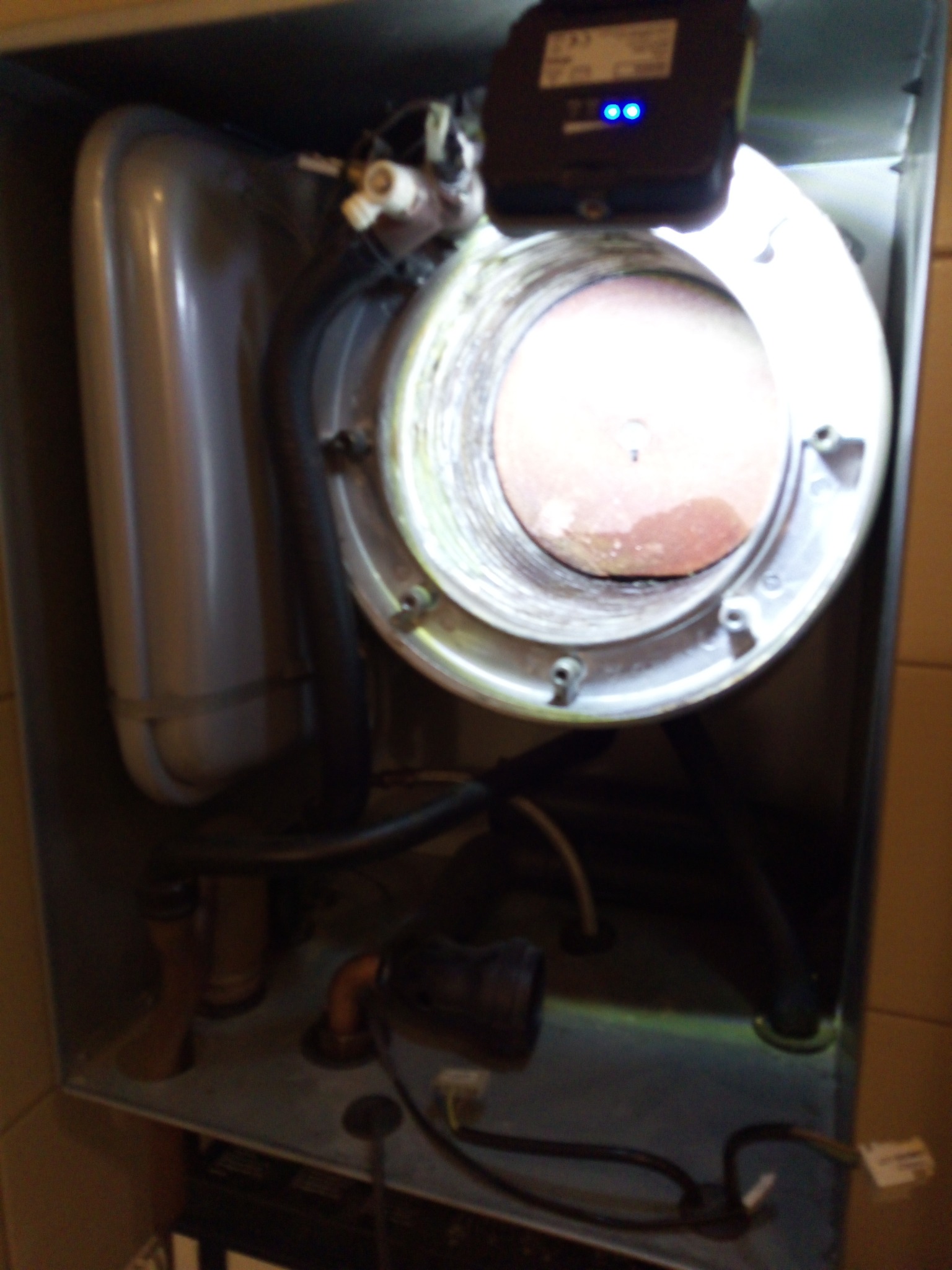 Wnętrze kotła gazowego z widocznymi elementami instalacji, rurami i elektroniką. Widoczne ślady użytkowania wewnątrz komory spalania. Oświetlenie LED na górze.