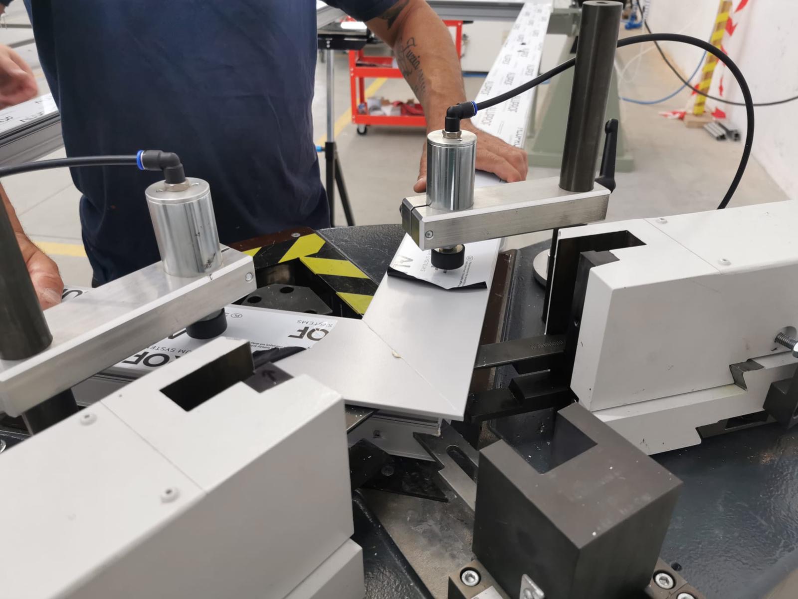 Proces łączenia profili aluminiowych na specjalistycznej maszynie. Widoczne elementy mocujące i fragment profilu z logo producenta.