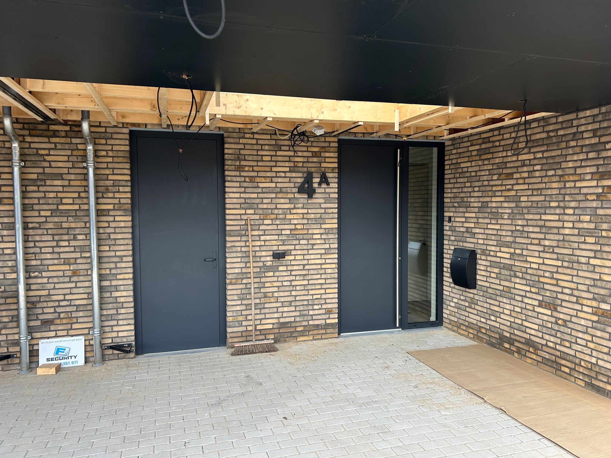 Dwa grafitowe wejścia do budynku z cegły klinkierowej, jedno z przeszkleniem. Widoczne rury spustowe, skrzynka na listy i numer domu '4A'.