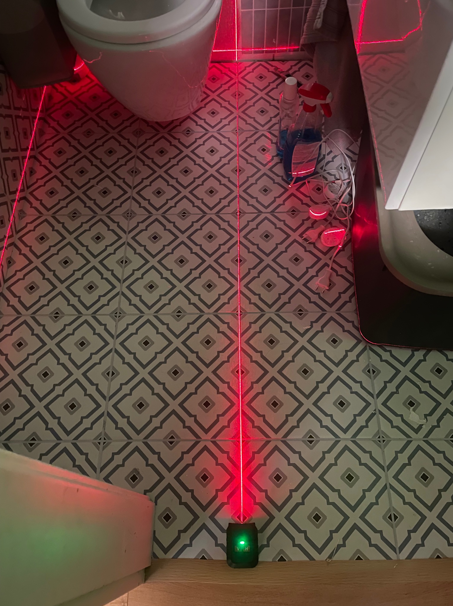 Ułożone płytki podłogowe w łazience w Białymstoku, wzór geometryczny, poziomica laserowa wyznacza linię. Widoczny fragment toalety i akcesoria łazienkowe.