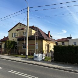 Sokół Budownictwo - Żółty dom jednorodzinny w trakcie remontu elewacji, z widocznymi rusztowaniami i workiem materiałów budowlanych. Czerwony dach i błękitne niebo w tle.