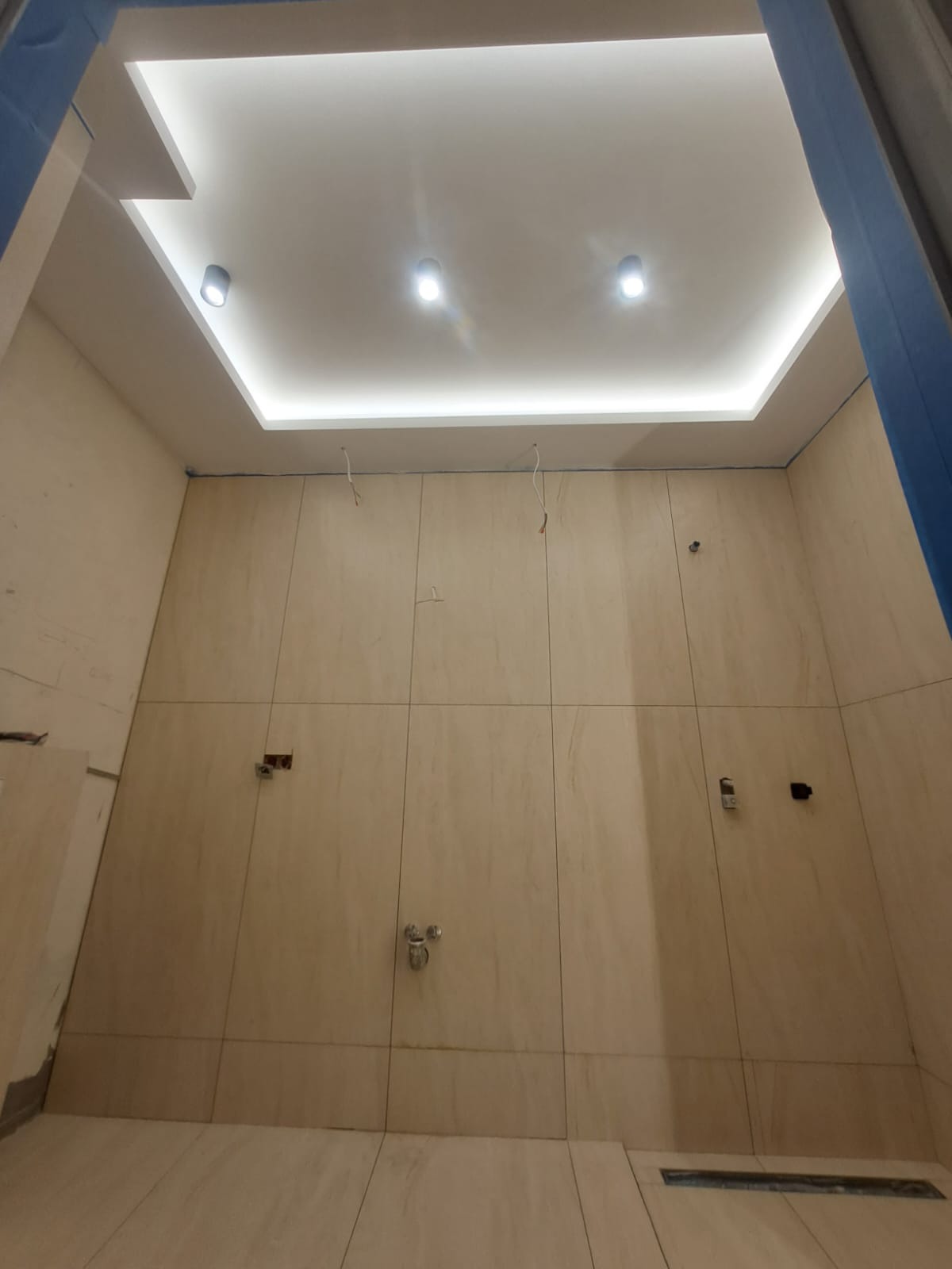 Wykończona łazienka z beżowymi płytkami, oświetleniem sufitowym LED i chromowaną armaturą. Widok z dołu podkreśla nowoczesny design i precyzję wykonania.