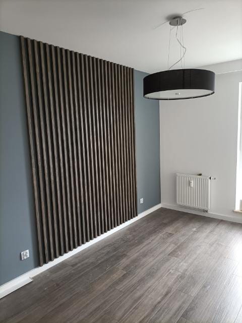 Nowoczesne wykończenie wnętrza: drewniane lamele na ścianie w odcieniach brązu, szara ściana, podłoga imitująca drewno i okrągła lampa sufitowa.