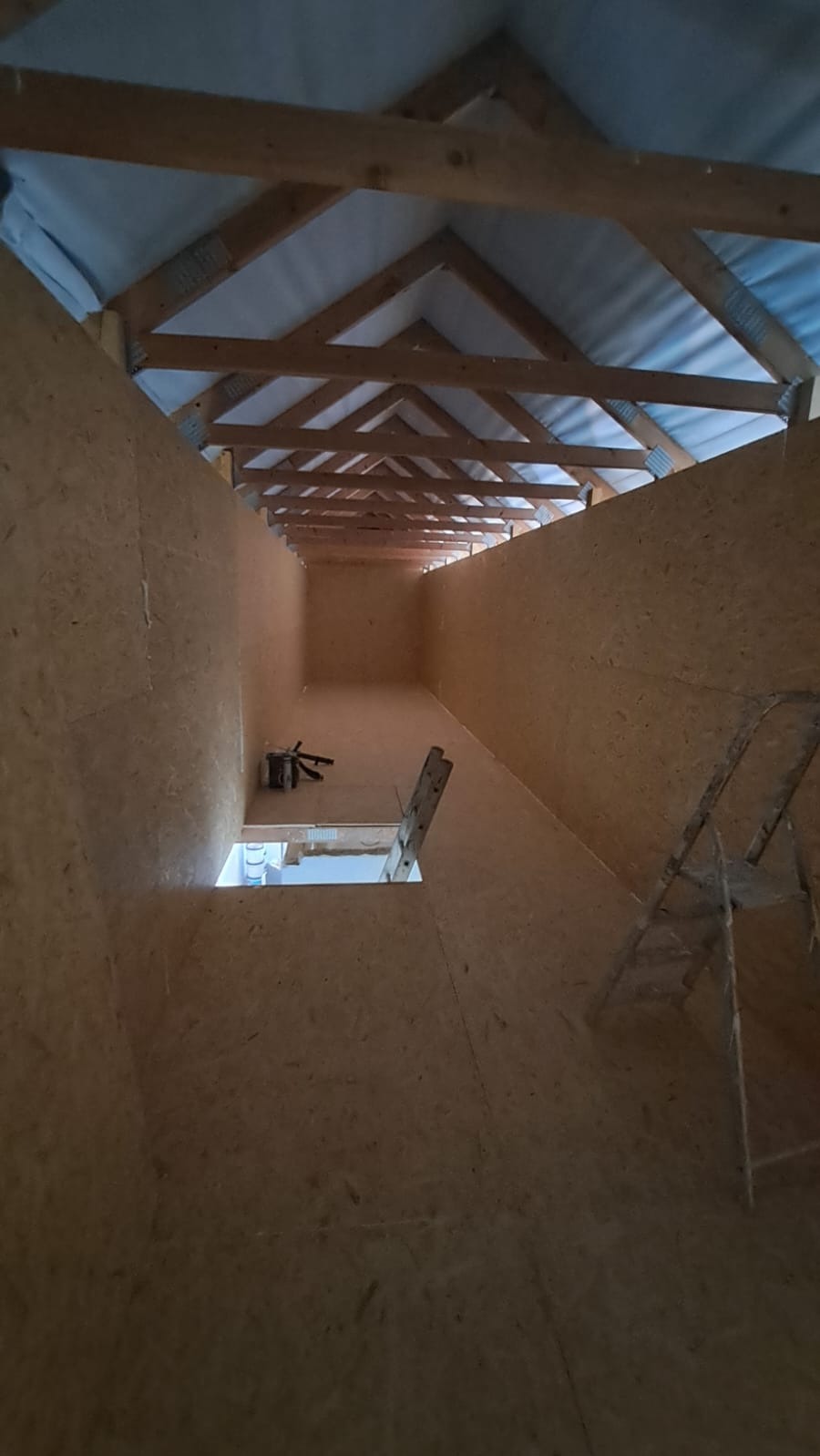 Wnętrze poddasza wyłożonego płytami OSB, widoczne drewniane krokwie i drabina. Przygotowanie do dalszych prac wykończeniowych, surowy stan.