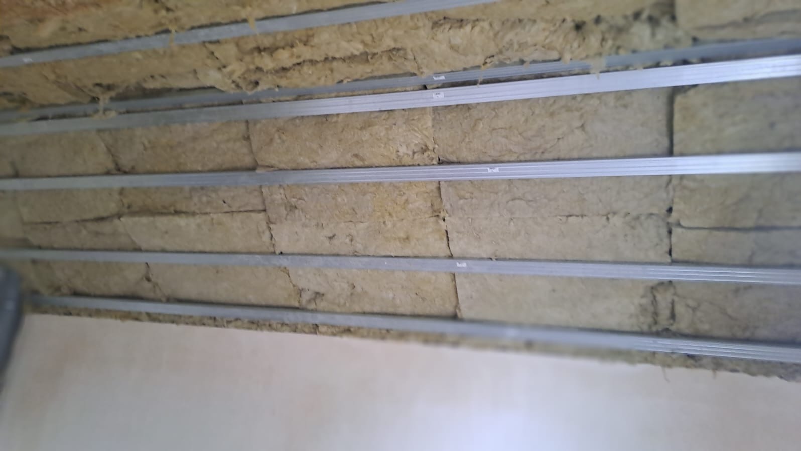 Izolacja z wełny mineralnej między metalowymi profilami sufitowymi, widok z dołu. Prace wykończeniowe wewnątrz budynku, oświetlenie dzienne.