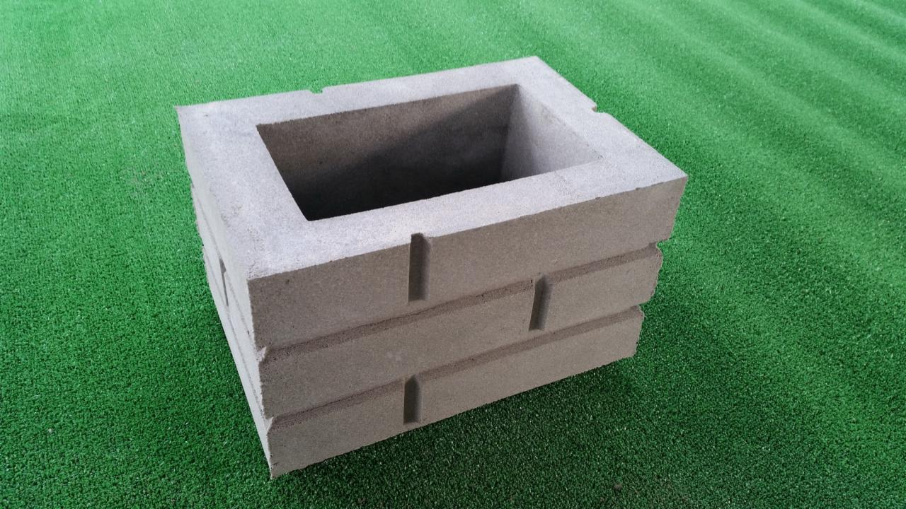 Betonowy element ogrodzeniowy w formie pustaka, imitujący cegłę, leżący na sztucznej trawie.
