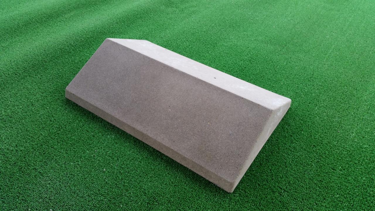 Betonowy prefabrykat na tle sztucznej trawy, element ogrodzenia z widoczną fakturą betonu.