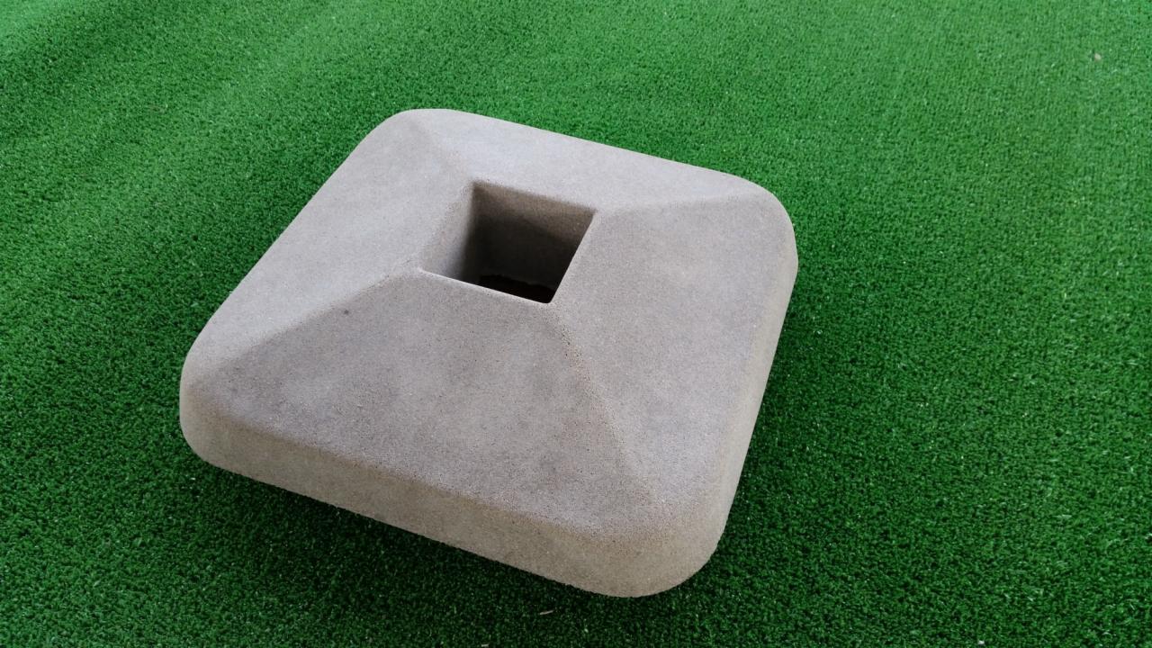 Betonowa podstawa słupka ogrodzeniowego z kwadratowym otworem na sztucznej zielonej trawie.