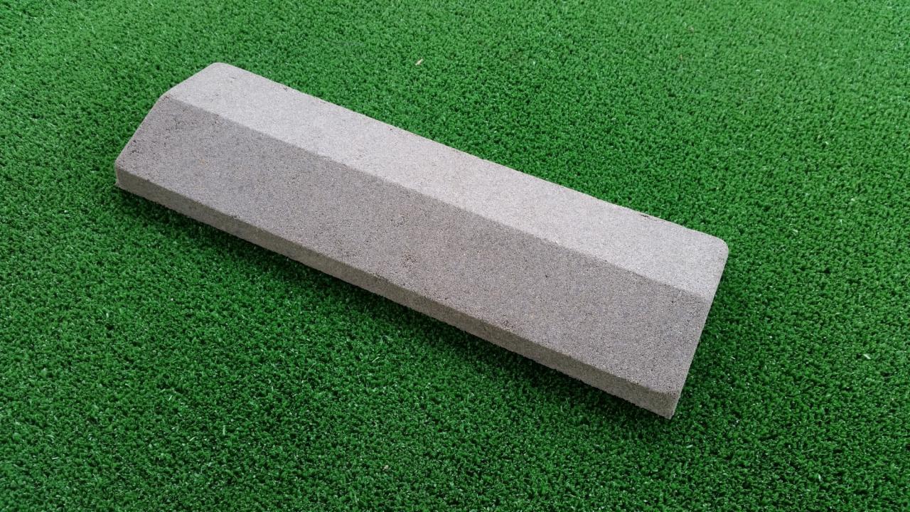 Szary, betonowy element ogrodzeniowy z fazowanymi krawędziami na zielonej sztucznej trawie.