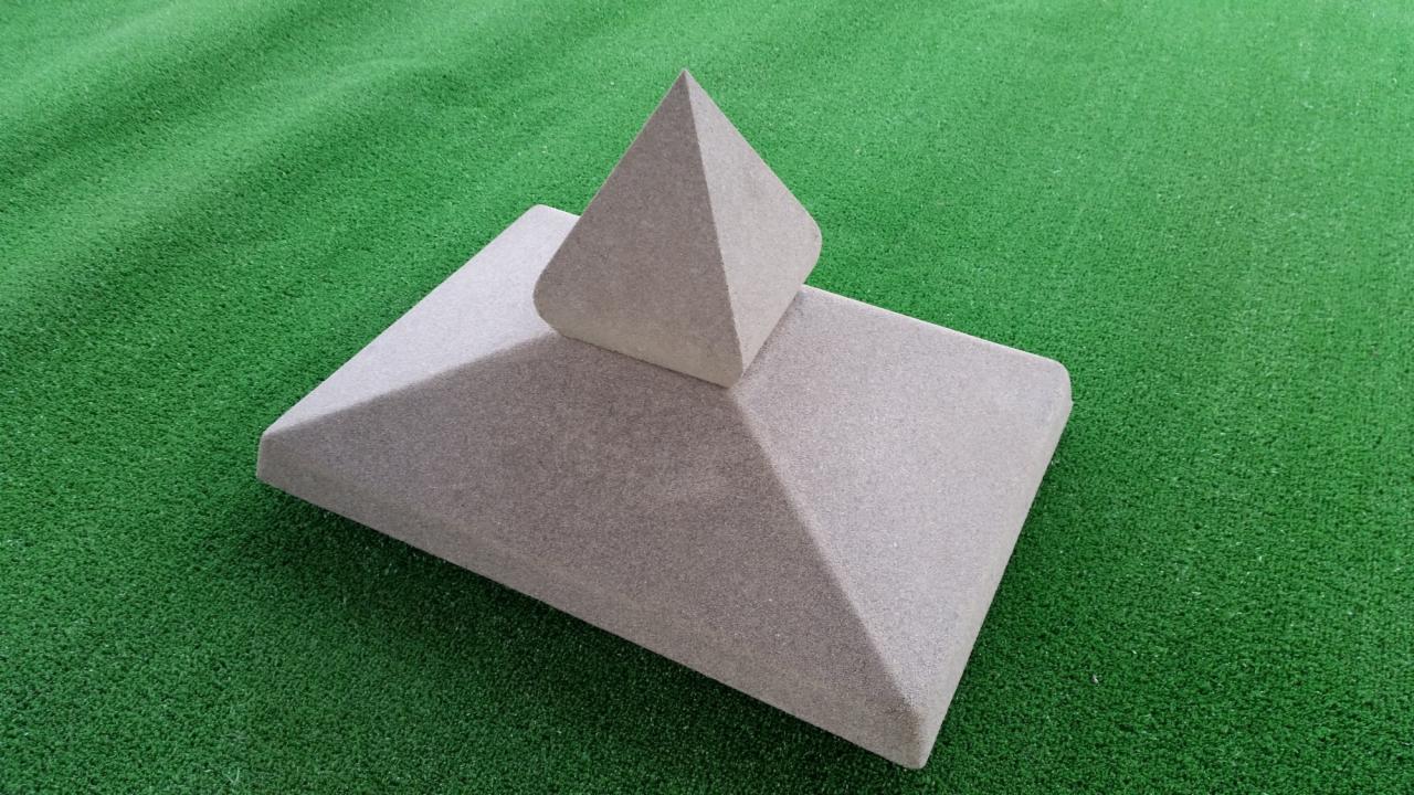 Betonowy słupek ogrodzeniowy z piramidalnym zwieńczeniem i oddzielna piramidka na tle sztucznej trawy.