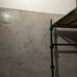 Usługi ogólnobudowlane - Ściana z efektem dekoracyjnym w odcieniach beżu, widoczny fragment rusztowania malarskiego. Wykończenie wnętrz z bliska, nieregularna faktura.